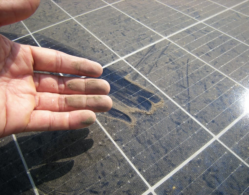 Close-up photo of a hand displaying dust and grime on a dirty solar panel, emphasizing the need for regular maintenance.