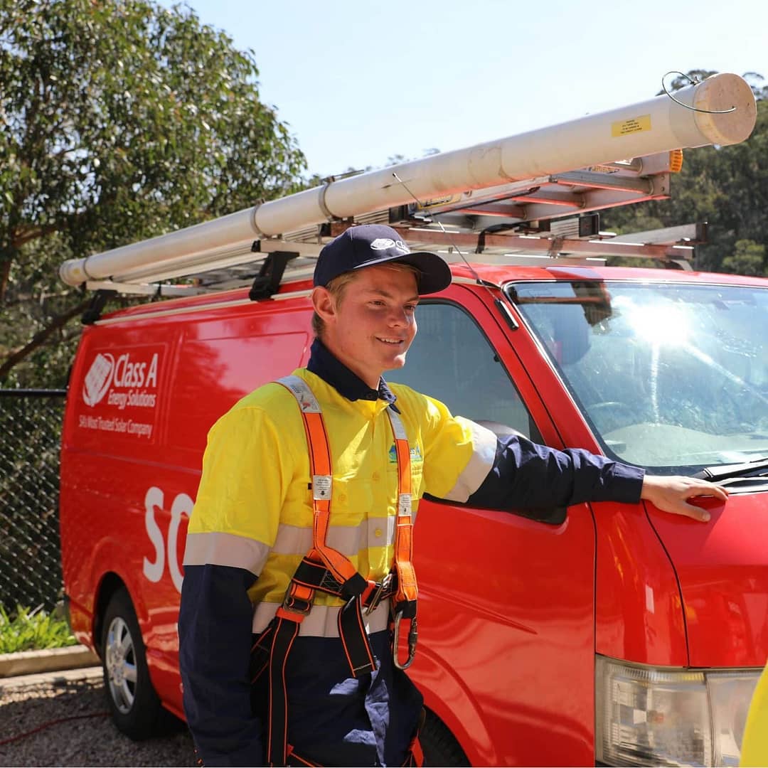Young apprentice electrician from Class A Energy Solutions standing next to a company van, discussing solar panel installation